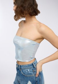 Top senza spalline di colore azzurro chiaro in materiale lucido, caratterizzato da un design aderente e una texture liscia, abbinato a pantaloni shorts in denim logorato.