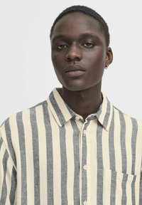 Camicia a righe in crema e blu navy, con design button-down, colletto e una singola tasca sul petto. Realizzata in tessuto testurizzato.