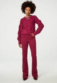 Maroon textuur trui met hartpatroon; ribbelboorden en -hals. Uitlopende maroon corduroy broek; gladde stof, aansluitend op de taille.
