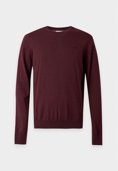 Pull à col rond à manches longues de couleur bordeaux foncé avec une taille ajustée et un logo discret sur la poitrine, présenté sur un fond uni.