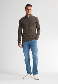 Maglione grigio scuro con collo a zip e motivo testurizzato, abbinato a jeans azzurri e sneakers bianche. Design minimalista, maniche lunghe.