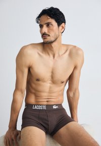 Rjave bombažne bokserice z belim pasom z logotipom "Lacoste", ki nudijo udoben oprijet fit in srednje visok dizajn. Gladka tekstura, minimalističen slog.