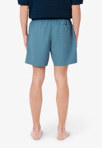 Pantaloni da bagno blu realizzati in tessuto leggero, dotati di una vita elastica e di una tasca sul retro destro, con una texture liscia.