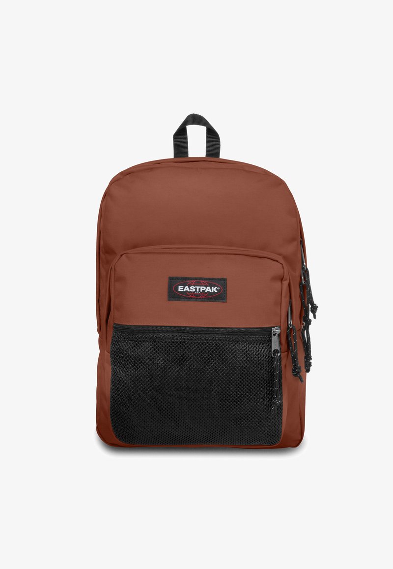 Brun tygväska med en svart meshlomme framtill; har ett handtag upptill och två dragkedjekläppar; logotypmärke placerat mitt på.