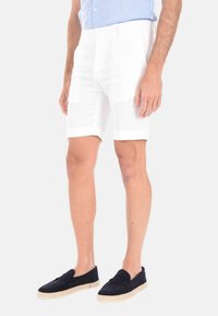 Pantaloni corti bianchi in lino con una vestibilità dritta e risvolti, abbinati a scarpe slip-on blu navy e una camicia button-up azzurra.