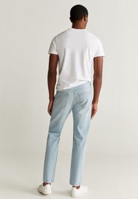 Camiseta de algodón blanca y jeans de mezclilla azul claro, corte clásico con bolsillos traseros. Usados con zapatillas blancas, fondo plano.