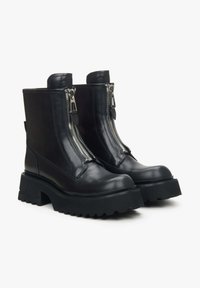 Zwarte leren enkellaarsjes met een chunky zool, twee voorkeursritsen en versterkte stiksels. Gladde textuur met een matte afwerking en een trekhaak.
