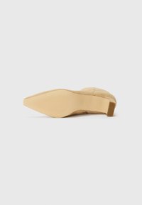 Beige suede heel with a smooth surface, pointed toe, and a textured, rubberized sole featuring horizontal ridges.