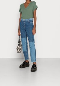 Top verde a maniche corte con scollo a V, jeans a vita alta in denim blu con patchwork, scarpe nere e una mini borsa a tracolla con motivo zebra.