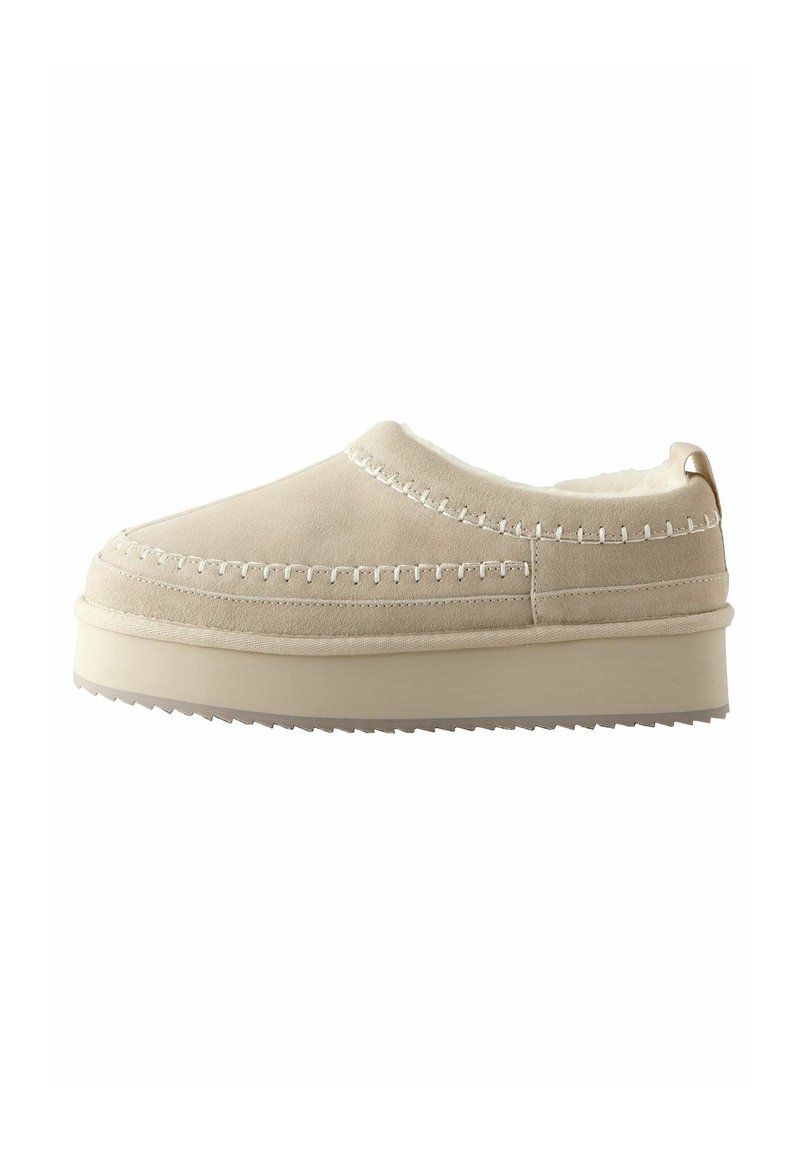 Beige sutsko med blød ruskindsøvre, hvide syninger og en tyk gummisål med en struktureret bund for bedre greb.