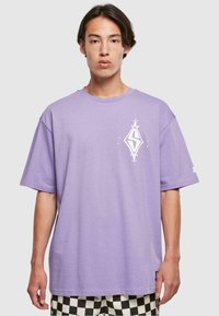 Purple cotton t-shirt with a loose fit, featuring a white graphic design on the chest and short sleeves. Paired with black-and-white checkered shorts.