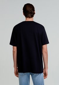 Sort kortærmet t-shirt lavet af bomuld, med en afslappet pasform, rund halsudskæring og synlige syninger på kanten.