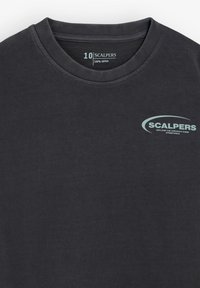 Camiseta de algodón gris oscuro con cuello redondo. Presenta un pequeño logo y texto "SCALPERS" en azul claro en el pecho. Diseño sencillo, sin estampados.