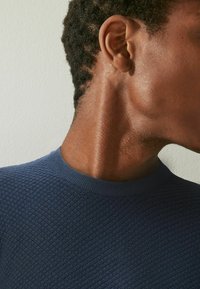 Pull texturé bleu marine avec un col rond, présentant une vue en gros plan de la peau et des cheveux, mettant en valeur la zone du cou et de l'épaule.