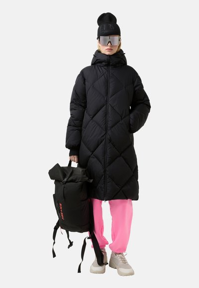 Zwarte doorgestikte gewatteerde jas met een hoge kraag, roze broek en een zwarte rugzak. Heeft een getailleerde taille, een gladde textuur en reflecterende accenten.