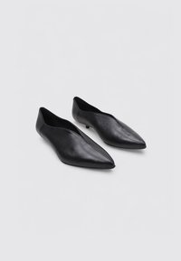 Chaussures noires en cuir à bout pointu au design épuré, avec un minimum de coutures et un petit talon pour une stabilité accrue.