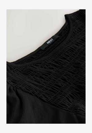 Top nero con design arricciato traforato frontale, tessuto liscio e scollo rotondo. L'etichetta riporta "NEXT".