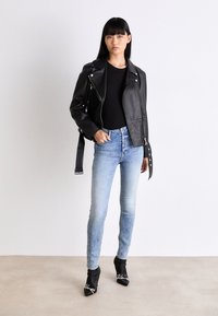 Svart läderbikerjacka med silverdetaljer, tillsammans med ljusblå skinny jeans. Modellen bär svarta ankelskor med vit text.