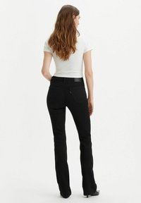 Svarta utsvängda jeans med åtsittande midja, bakfickor och subtila sömdetaljer. Tyget har en slät yta och lätt stretch.