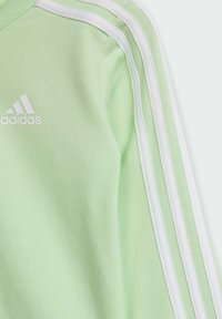 Felpa verde chiaro realizzata in tessuto morbido, con accenti a tre strisce bianche e logo adidas sul petto.