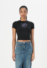 Černý krátký top s krátkým rukávem a fialovým grafikou s logem "TOMMY JEANS" ve tvaru srdce, doplněný modrou džínovou sukní s předními rozparky.