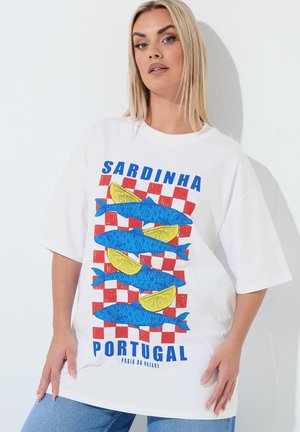 Vrouw met blond haar die een wit oversized T-shirt draagt met blauwe vissen en gele schijfjes citroen op een rood geruit achtergrond.