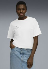 T-shirt en coton blanc à manches courtes et col rond, avec un imprimé noir sur la poitrine. Associé à une jupe en denim bleu clair.