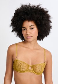 Sostén amarillo de encaje con un patrón floral, soporte con aro, bordes festoneados y tirantes ajustables. Presenta detalles en acabado dorado.