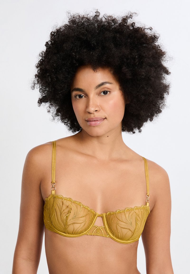 Sostén amarillo de encaje con un patrón floral, soporte con aro, bordes festoneados y tirantes ajustables. Presenta detalles en acabado dorado.