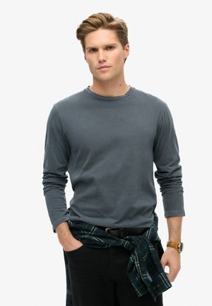 Grijze lange mouw shirt van katoen, met een ronde halslijn. Gepaard met donkere broek en een groen geruite flanellen stof om de taille geknoopt.