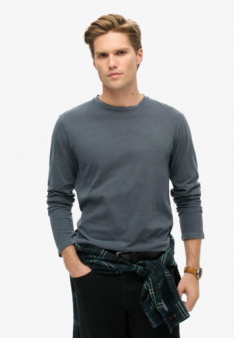 Grijze lange mouw shirt van katoen, met een ronde halslijn. Gepaard met donkere broek en een groen geruite flanellen stof om de taille geknoopt.