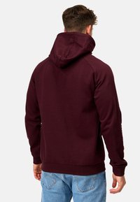 Haut à capuche bordeaux avec une grande capuche, des poignets et un ourlet côtelés. Le tissu semble doux et texturé, présentant un design sans couture et sans logos visibles.