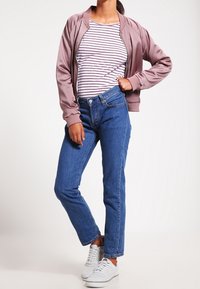 Ροζ bomber jacket πάνω από μπλούζα με ρίγες, συνδυασμένο με μπλε ίσια παντελόνια και λευκά αθλητικά παπούτσια.