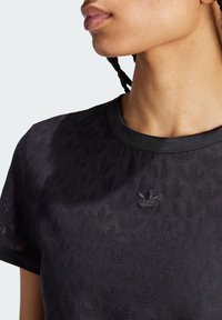 Fekete textúrált póló, diszkrét levélmintával és hímzett logóval a mellkasán. Kerek nyakkivágás és rövid ujjak.