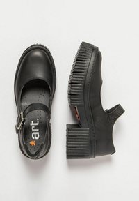 Zapatos de piel negra con un diseño tipo Mary Jane, correa ajustable, suela gruesa y ribeteada, y puntera redonda. La superficie es lisa con costuras mínimas.