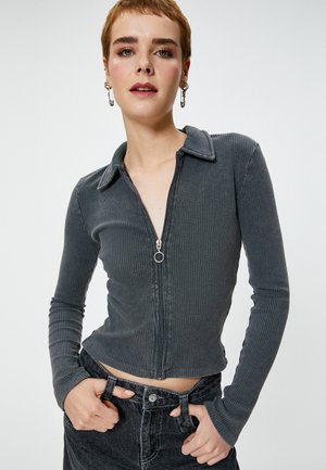 Geribbeld, met ritssluiting, lang mouwtop in donkergrijs met een kraag en een ronde ritssluitingaccent. Gecombineerd met zwarte high-waisted jeans.