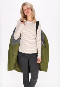 Olívazöld, puffosdzseki szürke béléssel, fehér és bézs csíkozott hosszúujjú póló fölött viselve. Fekete, slim fit farmernadrág.