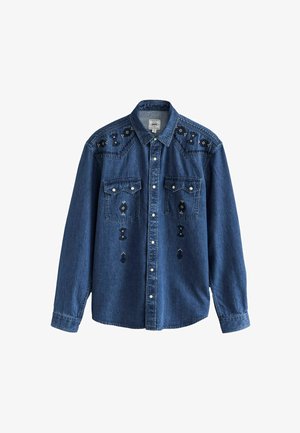 Sötétkék farmering fekete és ezüst díszítő szegecsökkal, két mellzsebbel, hegyes gallérral és gombos elülső résszel.