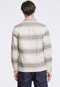 Maglietta a maniche lunghe color crema con strisce orizzontali grigie. Dotata di colletto e polsini con bottoni, realizzata in tessuto testurizzato.
