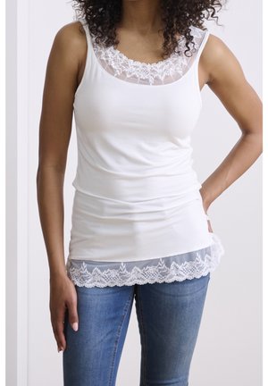 Top blanco sin mangas con escote y dobladillo de encaje transparente, que presenta una tela elástica y un corte holgado. Diseño clásico combinado con jeans de mezclilla.