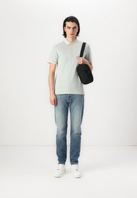 Polo shirt vert clair avec col contrastant, jean bleu, baskets blanches et sac bandoulière noir. Design simple et coupe décontractée.