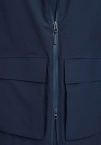 Mornarsko modra jakna s osrednjim zadrgo, dvema velikima sprednjima žepoma in gladko, mehko teksturo tkanine. Preprost dizajn, brez vidnih vzorcev ali dodatkov.