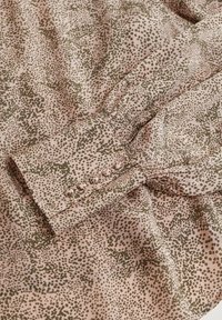 Blouse à manches longues en tissu rose clair ornée d'un motif de pois verts dispersés. Les détails notables incluent un poignet boutonné et une texture douce.