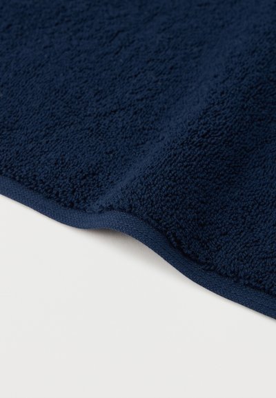 Tela de rizo azul oscuro con superficie texturizada y borde cosido cuidadosamente, extendida sobre un fondo blanco.