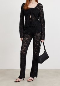 Svart spetscroptop med långa ärmar, tillsammans med matchande spetsbyxor. Har blommönster, genomskinlig textur och en figurnära silhuett.