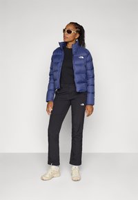 Námornícka pufrová bunda, čierny top a čierne nohavice. Svetlo sfarbené tenisky, štvorcové slnečné okuliare a viditeľné značkové doplnky. Hladká textúra, priliehavý strih.