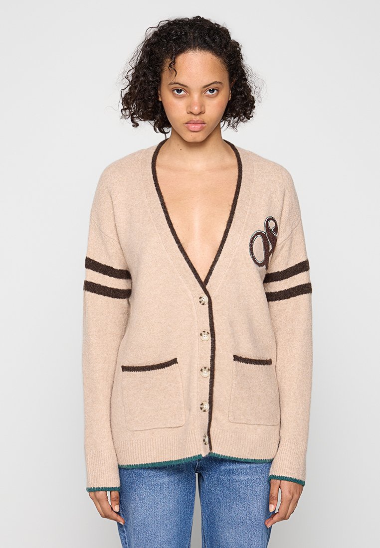 Beżowy dzianinowy kardigan z długimi rękawami, głębokim dekoltem w kształcie V, brązowymi paskami, dwiema przednimi kieszeniami i zapięciem na guziki. Zielony wykończenie u dołu.