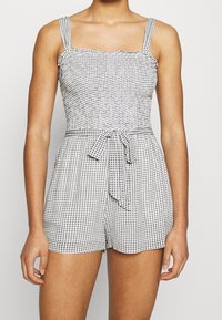 Romper a scacchi bianco e nero con scollo a quadrato, bordo arricciato e spalline regolabili. Include una vita con cintura e gambe corte.