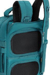 Turkusowy plecak materiałowy z siateczkowymi kieszeniami, wyściełanymi paskami i zamkami błyskawicznymi; charakteryzuje się usztywnionym kształtem z regulowanymi klamrami i akcentami z metalowych elementów.