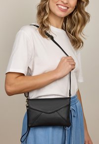 Schwarze Leder-Umhängetasche mit einem Umschlagdesign, strukturiertem Finish, rechteckiger Form und verstellbarem Tragegurt.